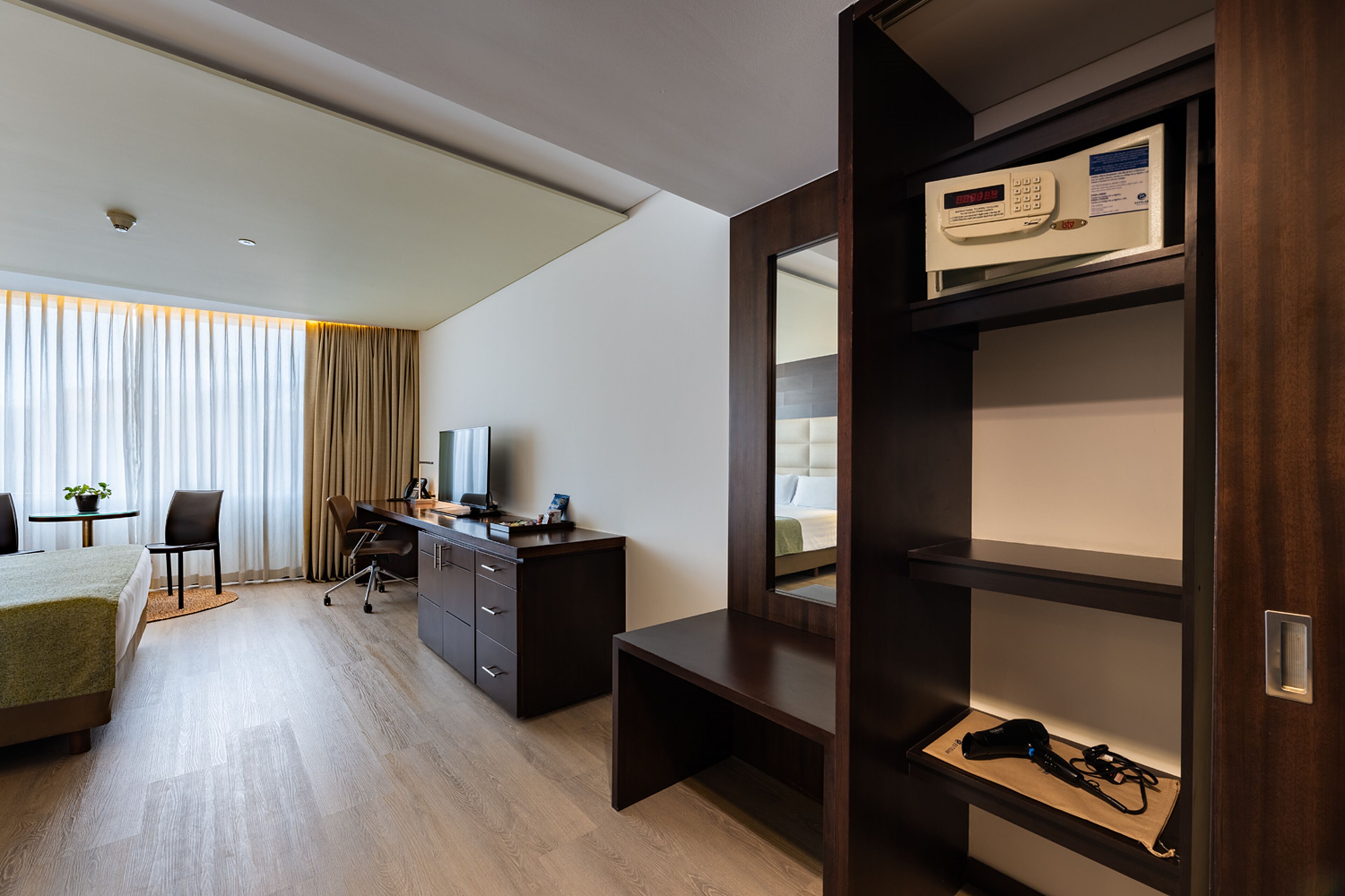 Una habitación de hotel con cama, escritorio, silla y armario con espejo.