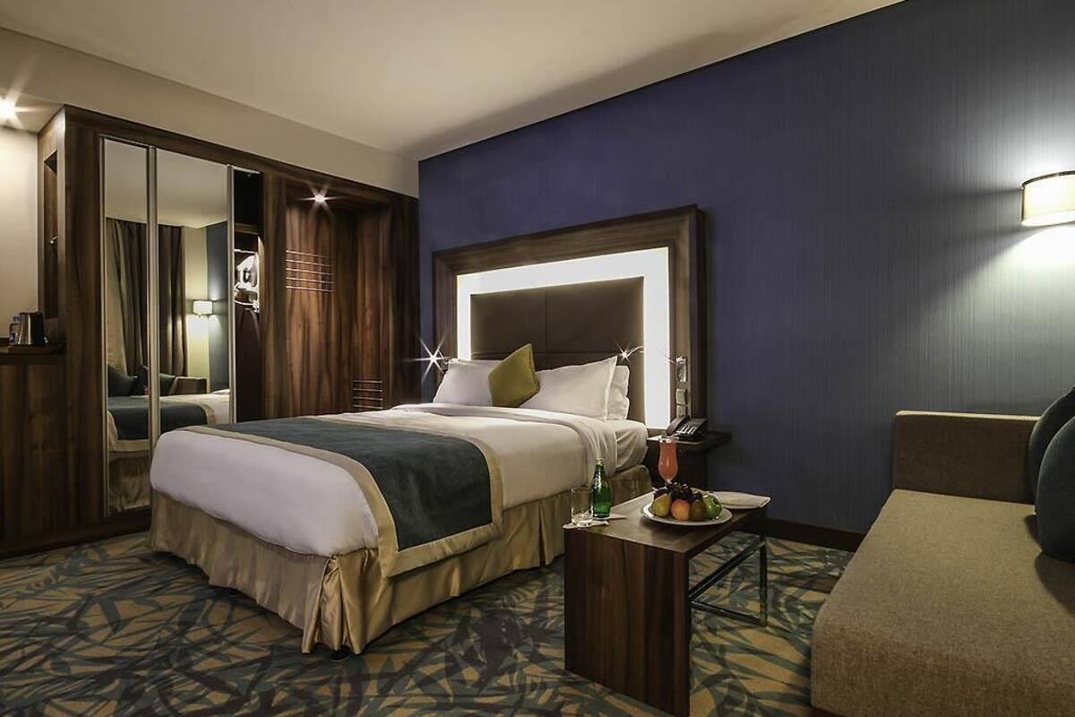 A hotel room with a large bed, a bedside table with a lamp, a chair, and a mirror.