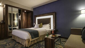 A hotel room with a large bed, a bedside table with a lamp, a chair, a mirror, and a wardrobe.