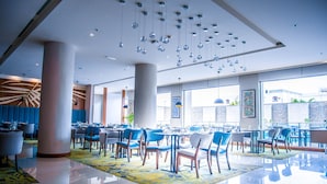 A modern restaurant with a clean, spacious layout, featuring blue chairs and tables, large windows, and hanging spherical light fixtures. - Novotel Yanbu (Yanbu)