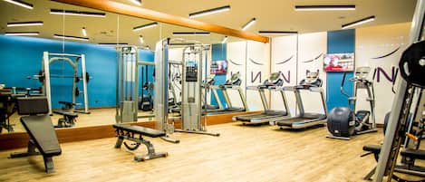 Une salle de sport équipée de divers appareils d’exercice, dotée d’un plancher en bois et d’un mur bleu.
