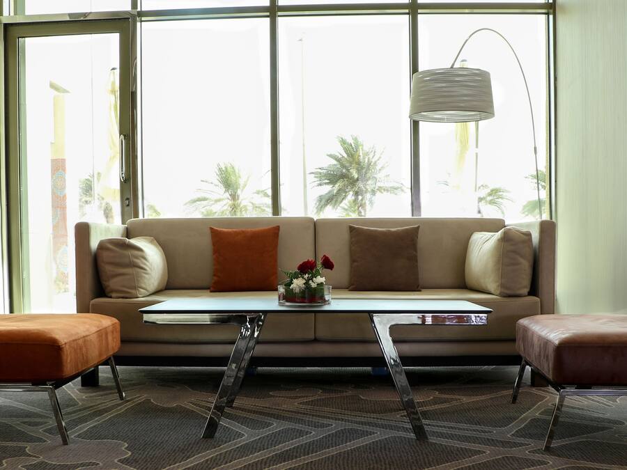 Una sala de estar moderna con un sofá, dos sillones, una mesa de centro y vistas a palmeras a través de amplios ventanales.