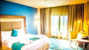 A hotel room with a large bed, a desk, a chair, and a window with curtains.