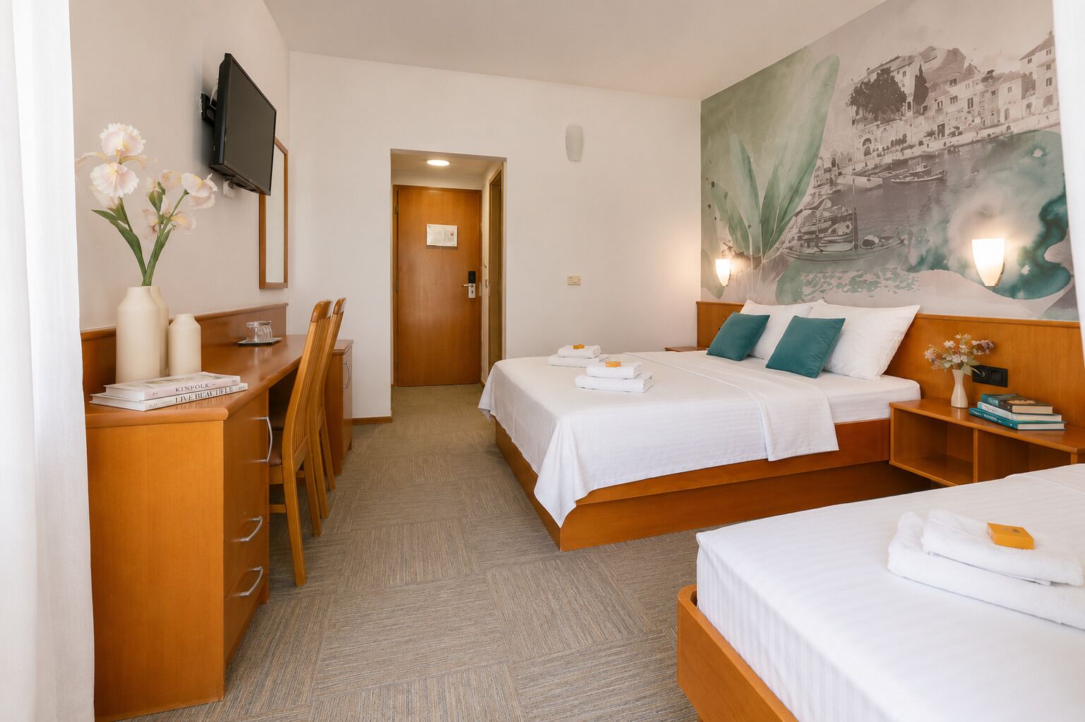 A hotel room with a bed, bedside tables, a desk, a chair, a TV, and a painting on the wall.