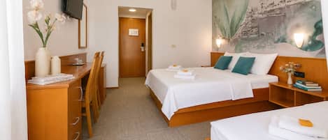 A hotel room with a bed, bedside tables, a desk, a chair, a TV, and a painting on the wall.