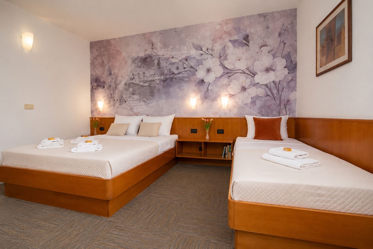 Une chambre d’hôtel avec deux lits, une grande fresque murale à motifs floraux et une petite bibliothèque.
