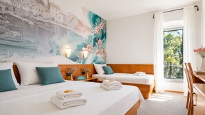 Habitación de hotel con dos camas, un mural grande, un balcón con vistas y un escritorio con una silla.