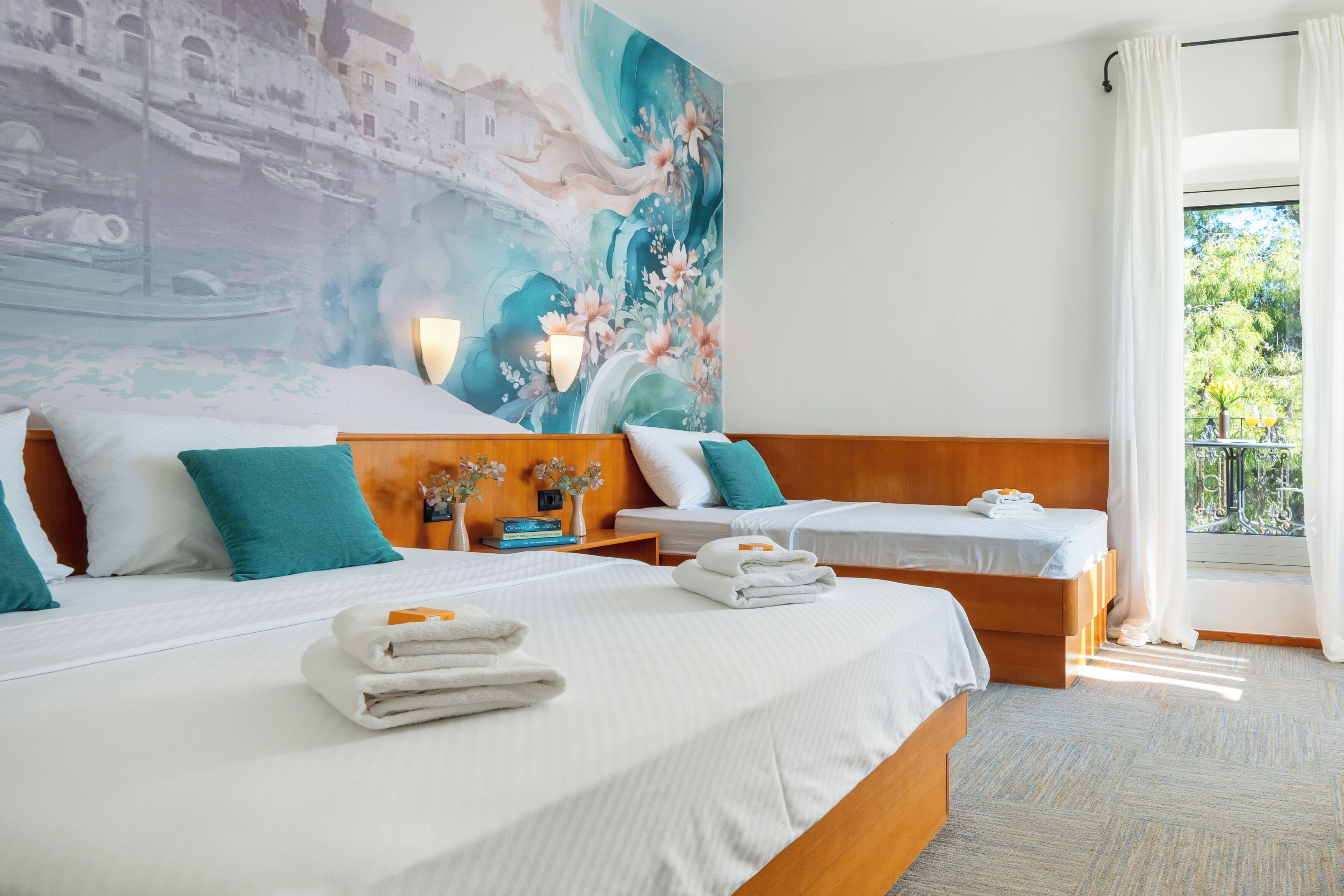 A hotel room with two beds, a large mural on the wall, a balcony with a view, and a neatly made bed with towels.