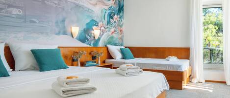 A hotel room with two beds, a large mural on the wall, a balcony with a view, and a neatly made bed with towels.