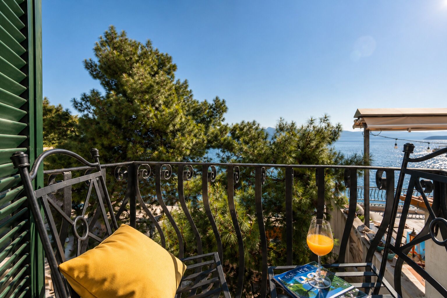 A balcony with a view of the sea, a yellow cushion, and a glass of orange juice.