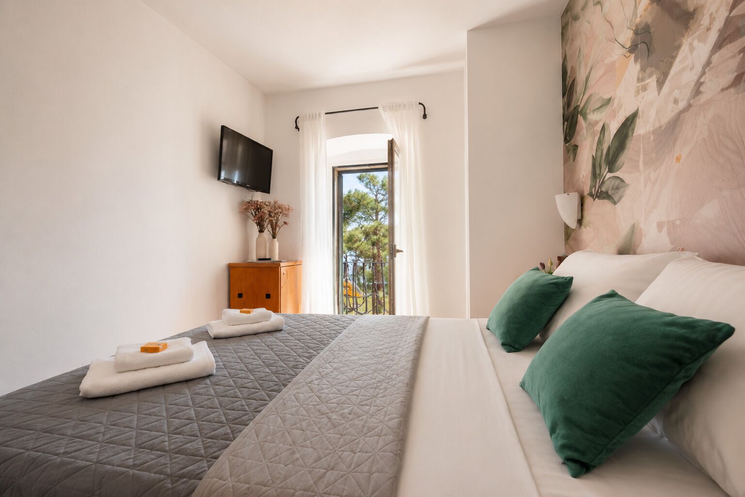 A bedroom with a bed, a TV, a wooden cabinet, and a balcony view.