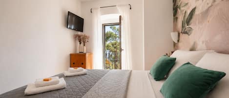 A bedroom with a bed, a TV, a wooden cabinet, and a balcony view.