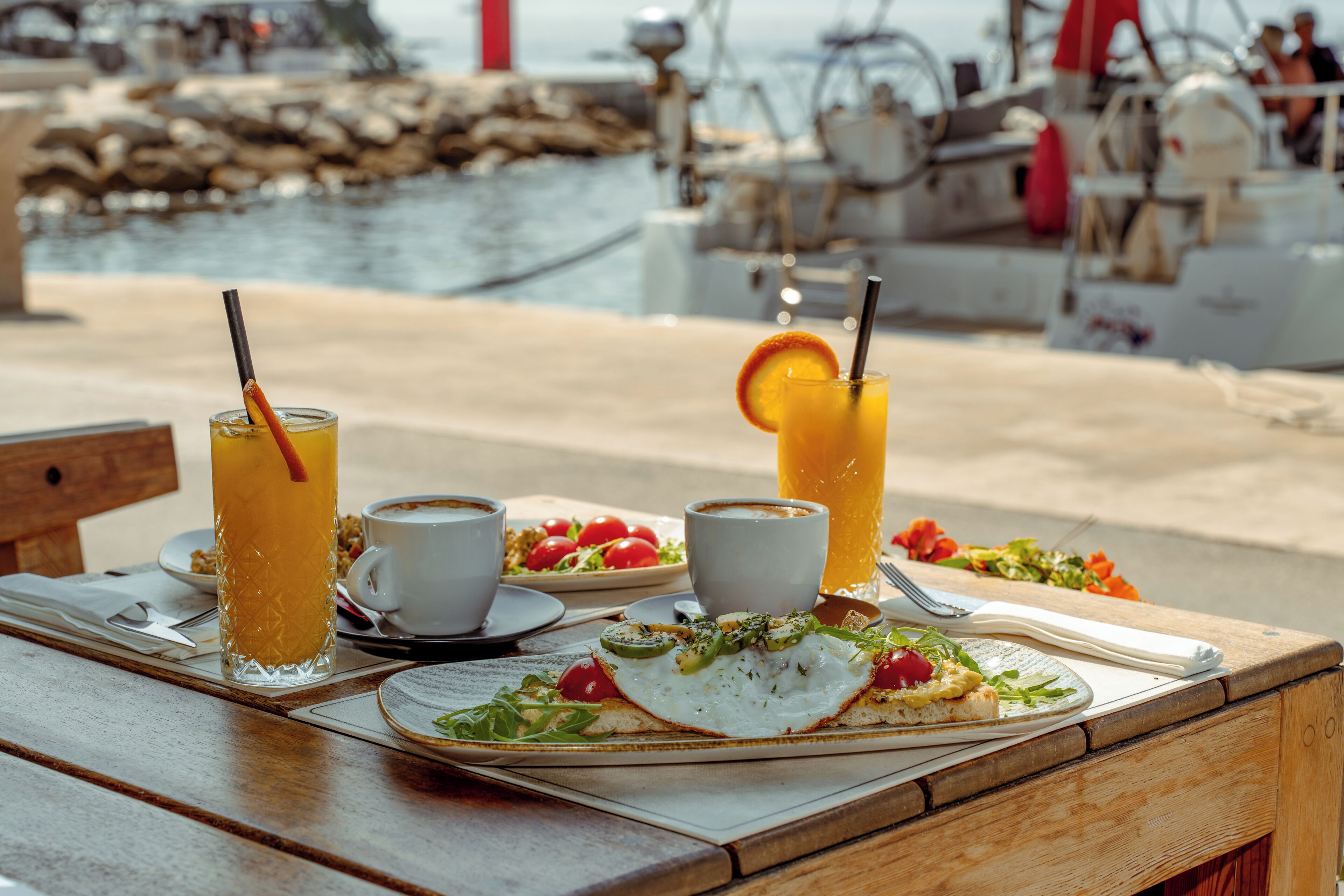 Une table en bois dressée pour le petit-déjeuner, avec une assiette de nourriture, deux verres de jus d’orange et deux tasses de café.