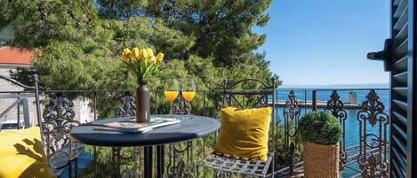 A balcony with a round table, yellow cushions, a wicker planter, and a view of the sea.