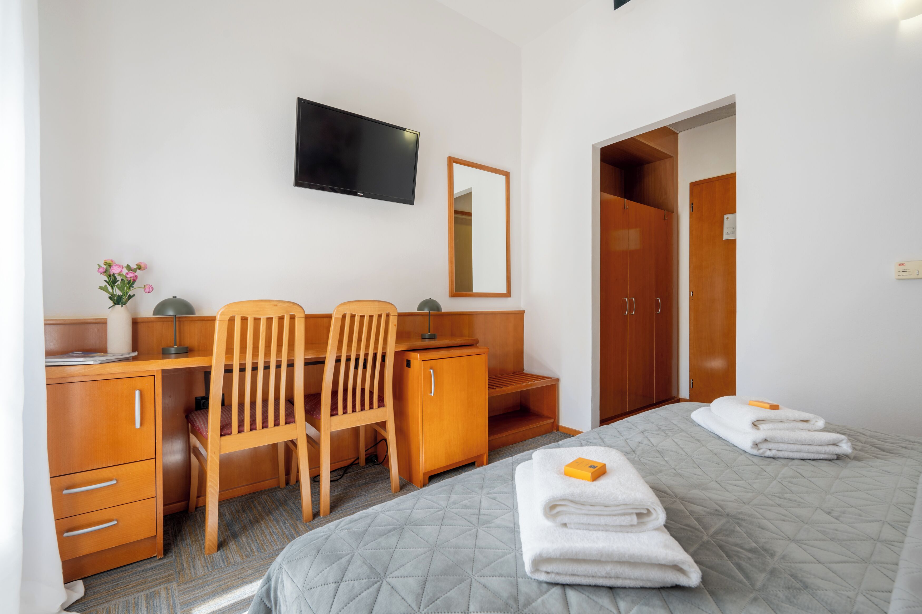 Een hotelkamer met een bed, een bureau met stoel, een televisie, een kledingkast en een spiegel.
