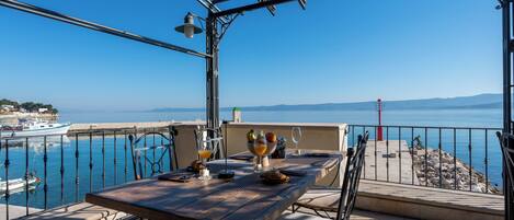 A terrace with a table set for breakfast overlooking a marina and the sea.
