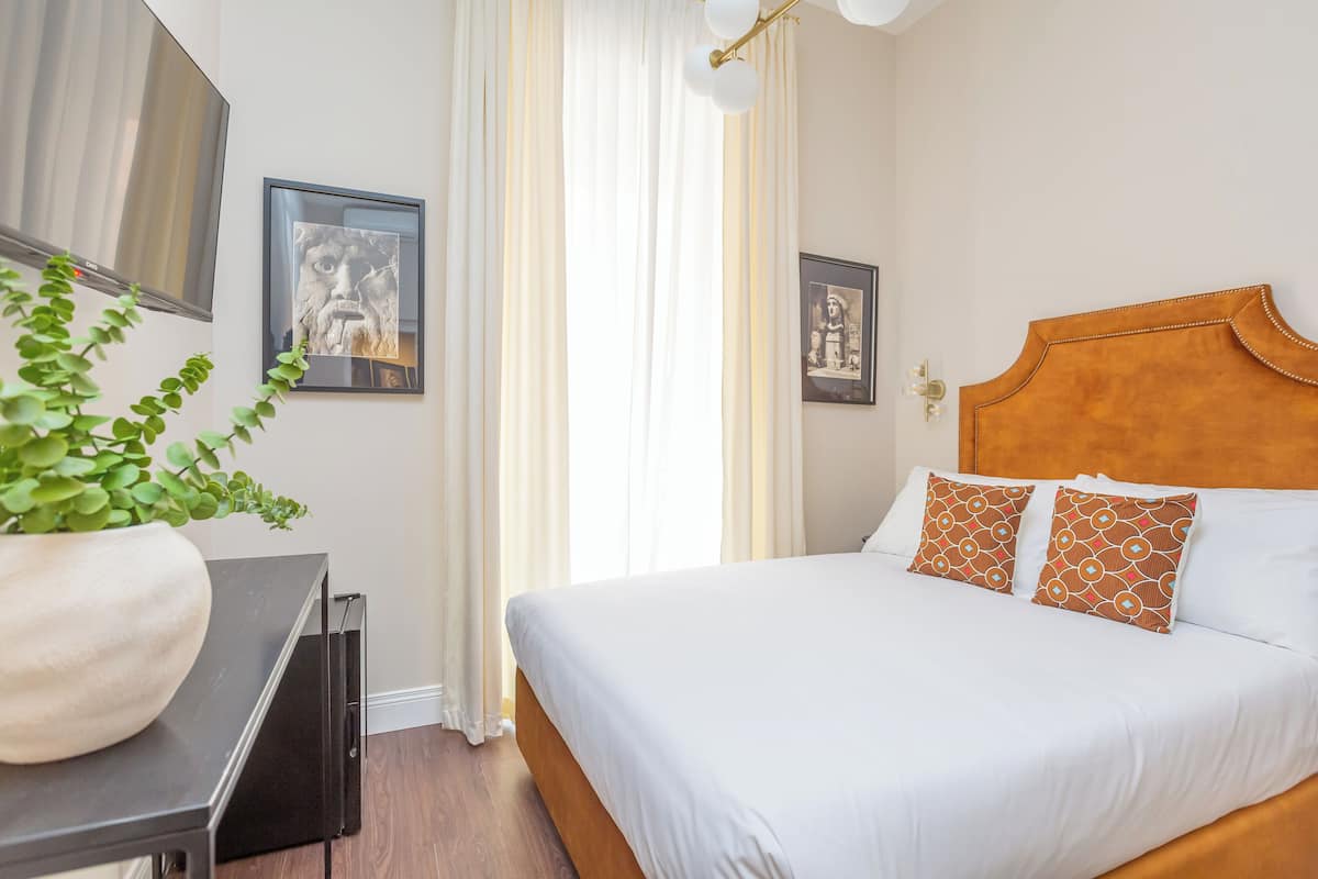 A neatly made bed with white and patterned pillows, a wooden headboard, and a potted plant on a bedside table.