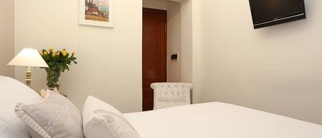 Habitación de hotel con una cama, televisión montada en la pared, una lámpara y una silla.
