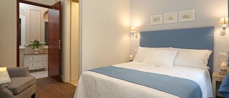 A bedroom with a large bed, a bedside table with a lamp, a dresser, and a chair.