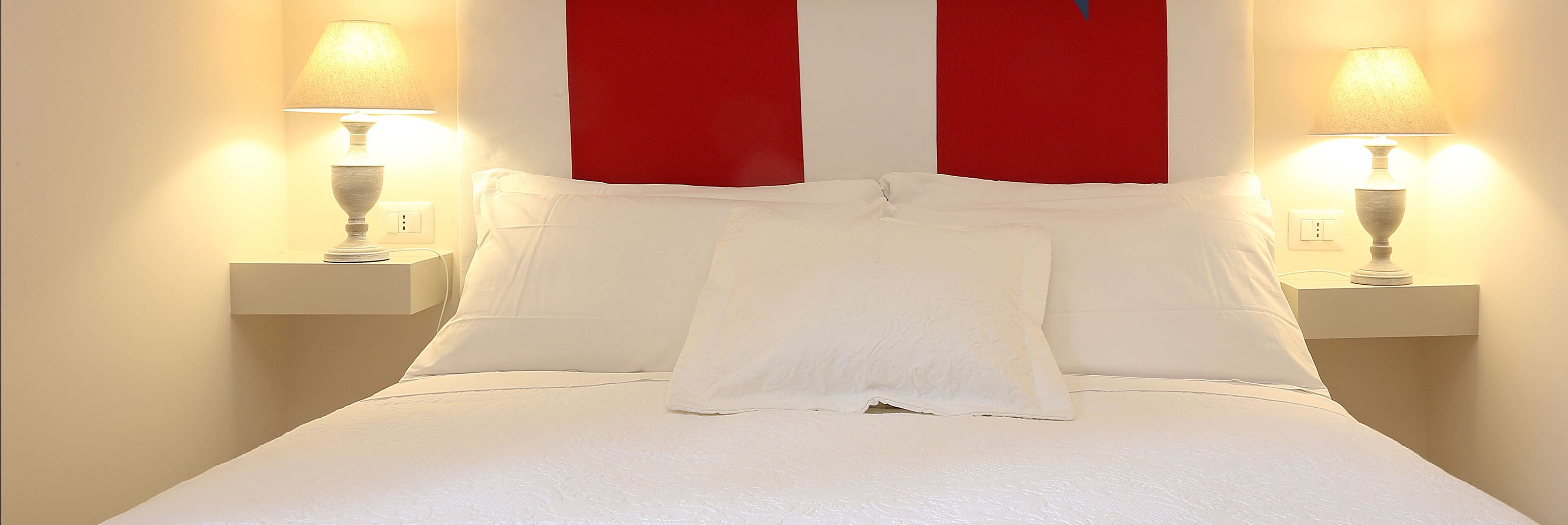 A neatly made bed with white linens and pillows, flanked by two bedside lamps on matching nightstands.