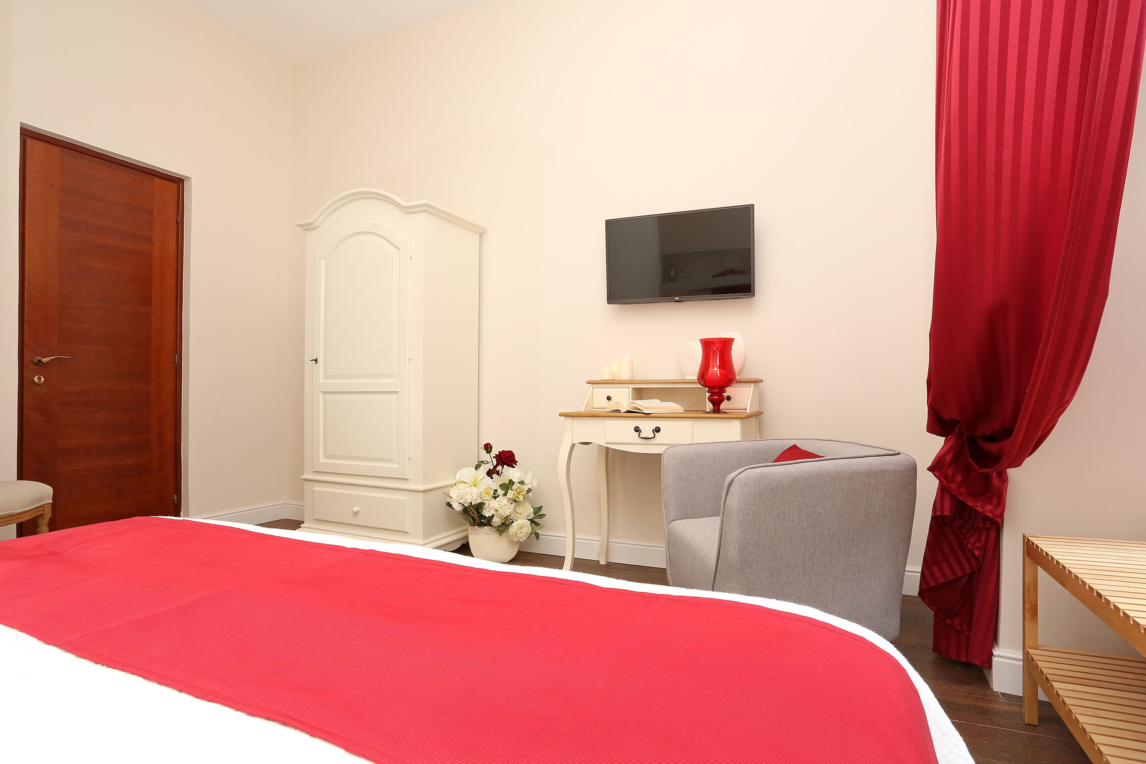 A bedroom with a bed, a wardrobe, a desk, a TV, and a red curtain.