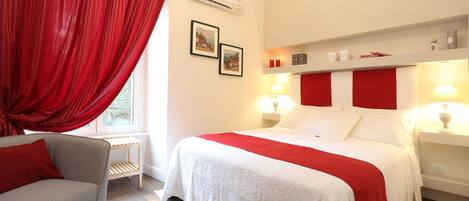 A hotel room with a bed, a chair, a bedside table, and a window with curtains.