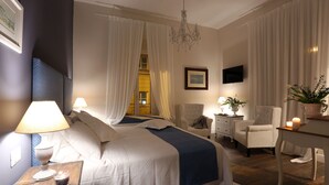Un dormitori amb un llit gran, dues taules de nit, una cadira, un escriptori i una televisió.