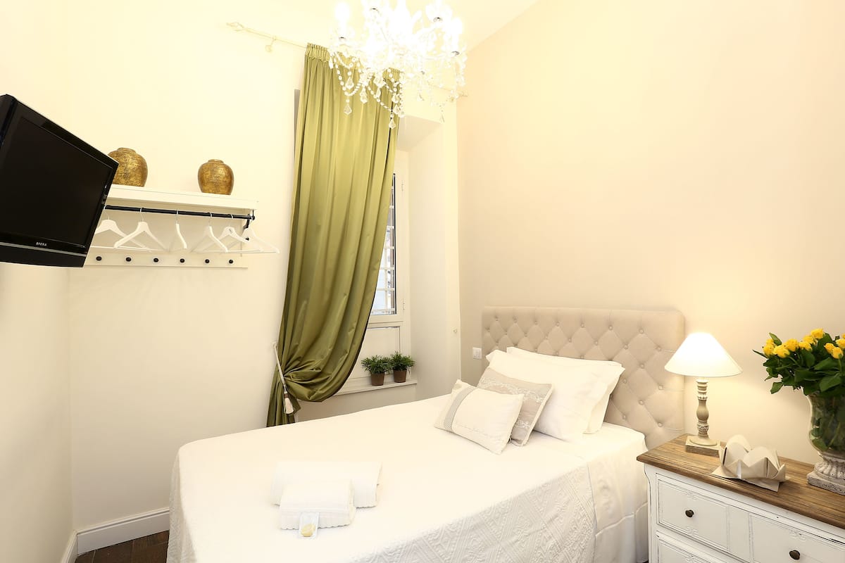 A neatly arranged bedroom with a bed, bedside table, lamp, and a TV mounted on the wall.