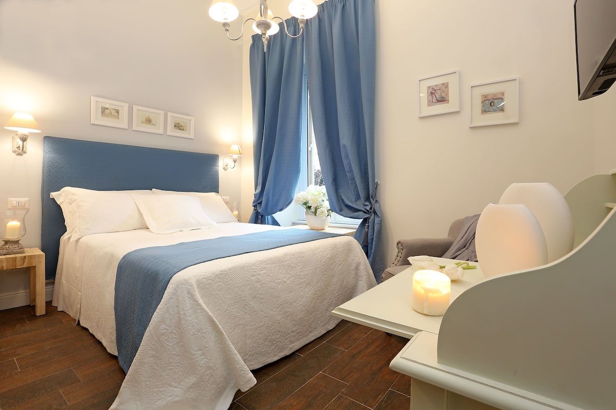 A neatly arranged bedroom with a bed, bedside table, lamp, and a small table with a candle.