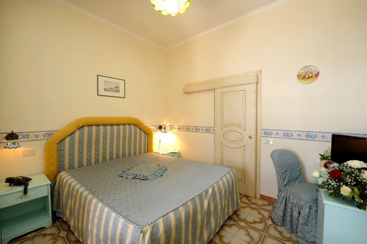 A bedroom with a bed, bedside table, lamp, chair, and a door.