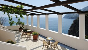 A terrace with white columns, potted plants, wicker chairs, and a view of the sea. - Locanda Del Fiordo (Furore)