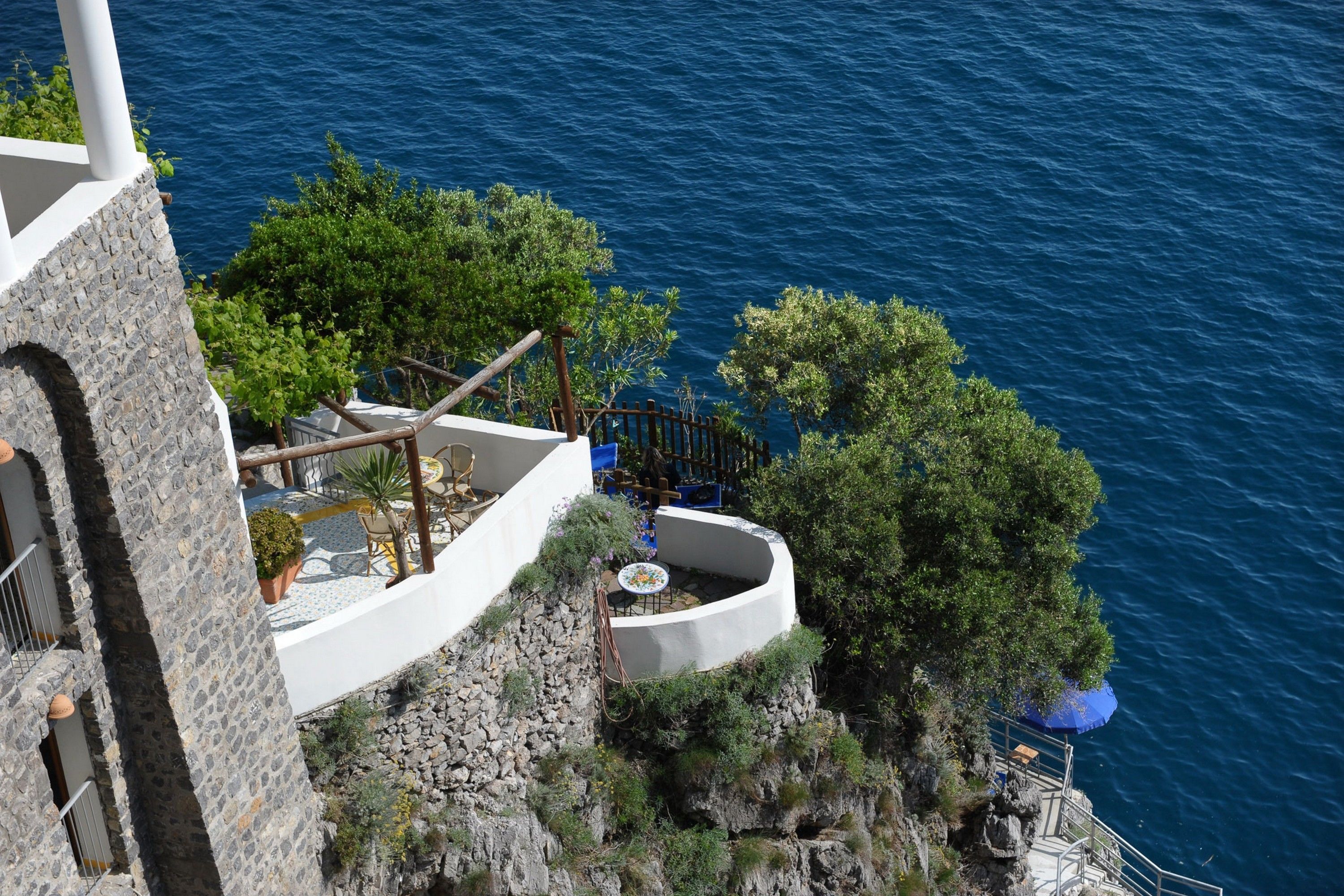 A seaside terrace with a stone wall, a curved seating area, and a view of the sea.