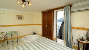 A bedroom with a large bed, a wooden door, a small table with a lamp, and a view of the outdoors. - Locanda Del Fiordo (Furore)