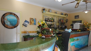 A hotel reception area with a green marble counter, a painting of a coastal scene, and a variety of decorative items including a floral arrangement. - Locanda Del Fiordo (Furore)