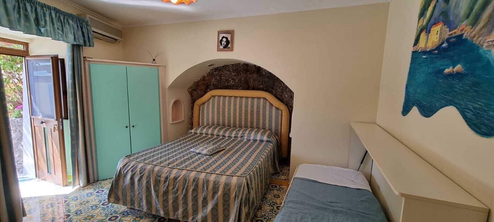 A bedroom with a bed, a wardrobe, a small table, and a painting on the wall.
