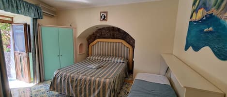 A bedroom with a bed, a wardrobe, a small table, and a painting on the wall.