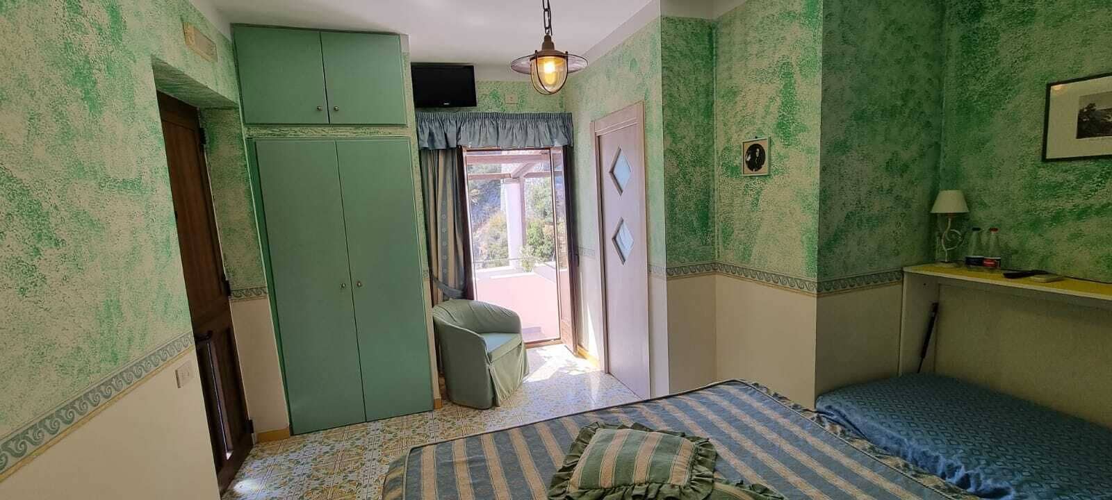 Una habitación con cama, armario, una mesita de noche con lámpara y vistas al exterior.