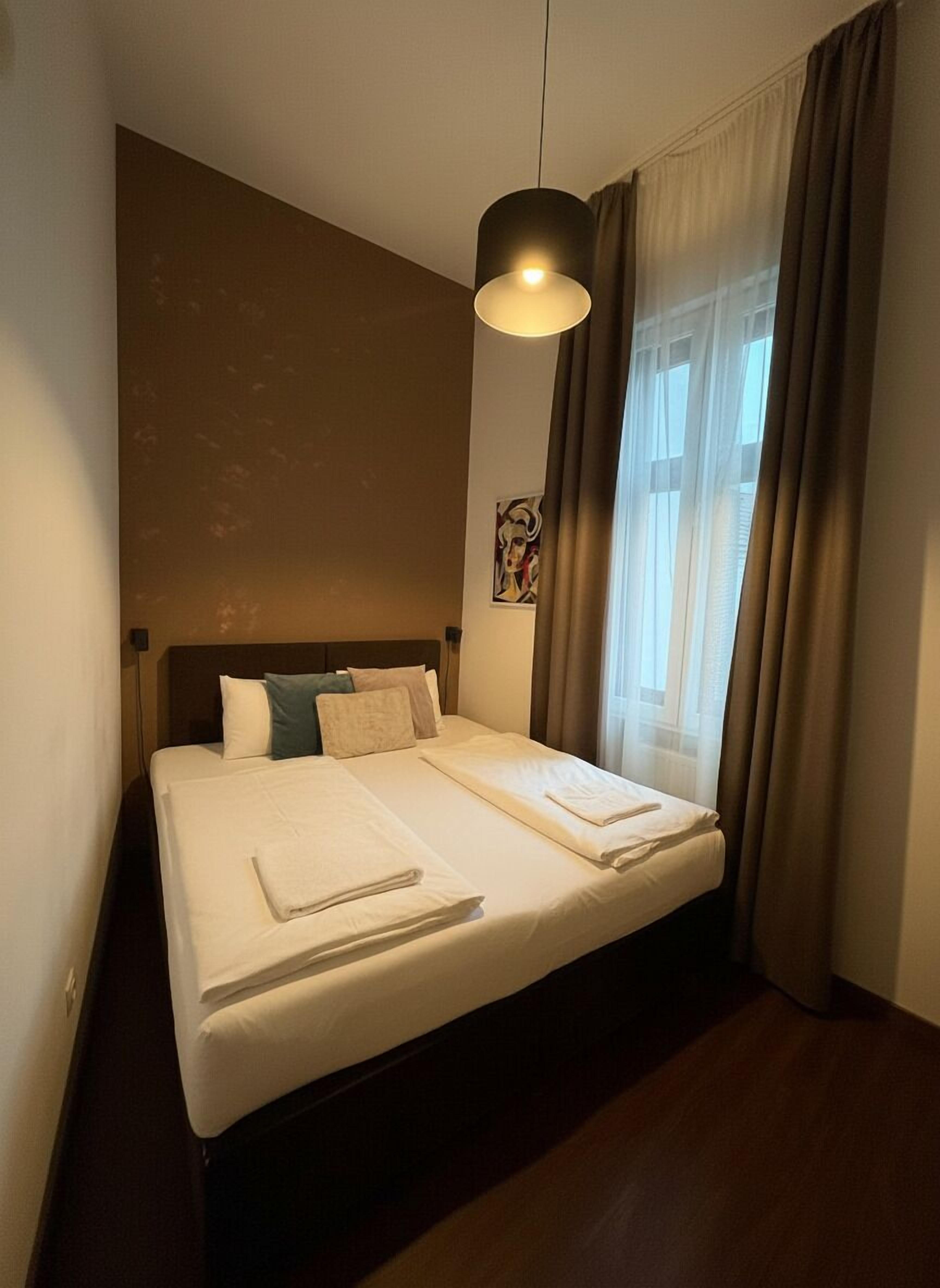 A neatly made double bed with white linens, a headboard, and a hanging light fixture.