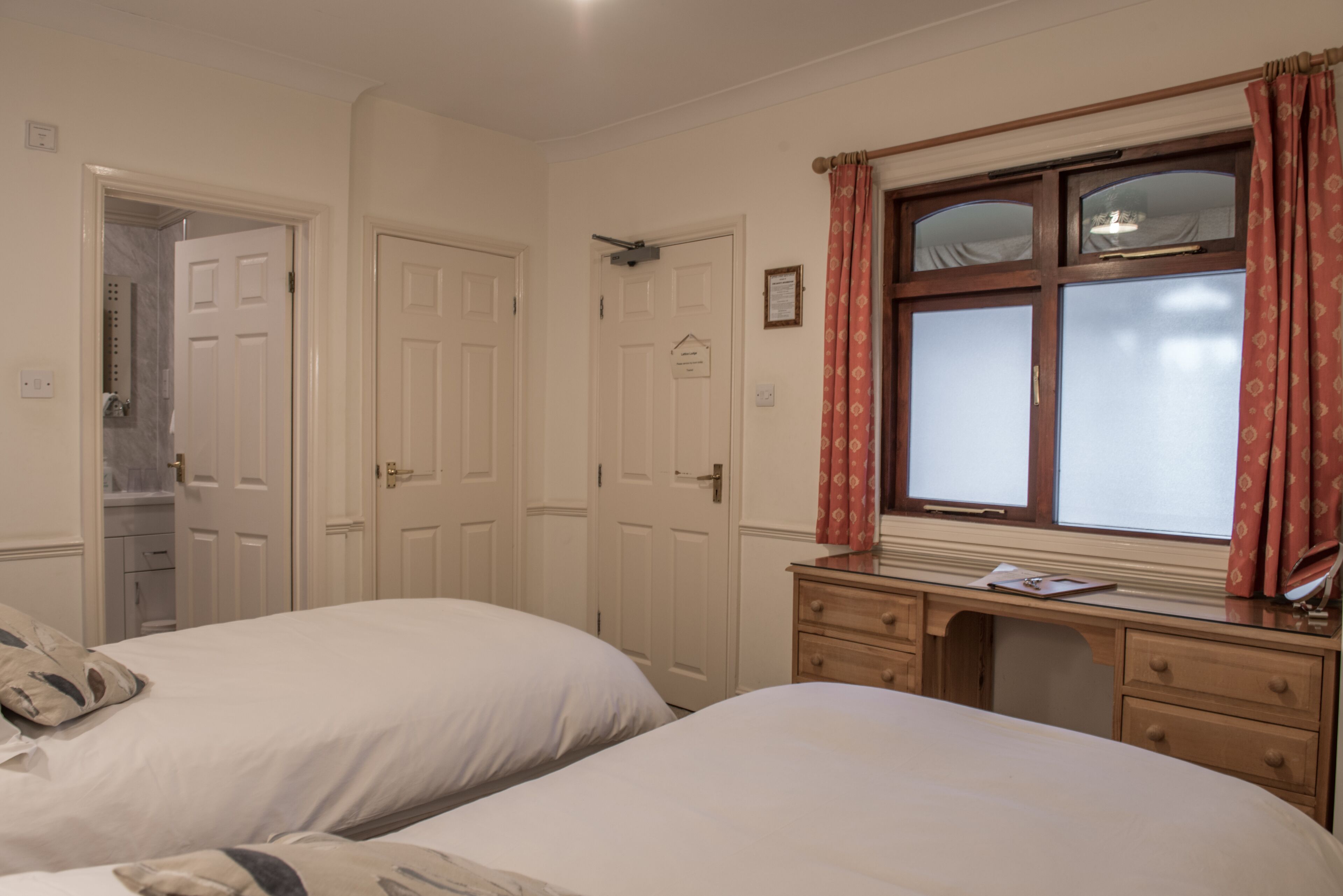 A bedroom with two beds, a desk, and a window with curtains.