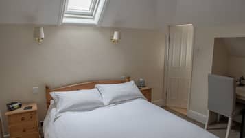 A neatly made bed with white linens, a bedside table with a lamp, a small bedside table with a phone, and a chair with a checkered pattern.