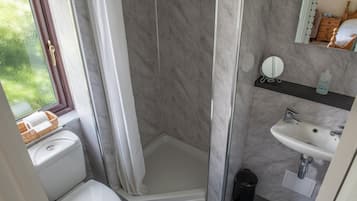 Un baño con ducha, inodoro, lavamanos y ventana con vistas a la vegetación.