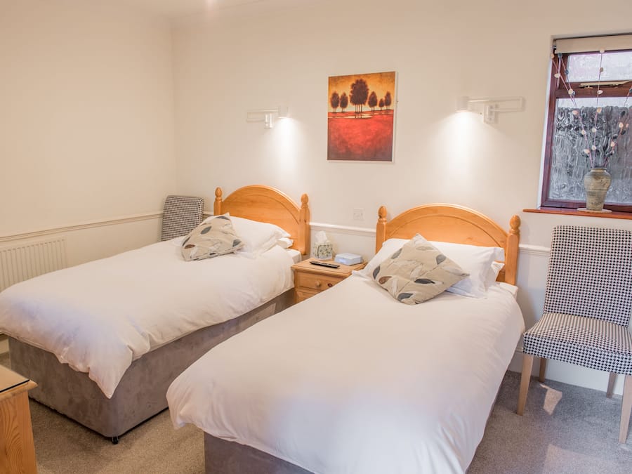 A twin room with two single beds, a bedside table with a lamp, a chair, and a window with a view.