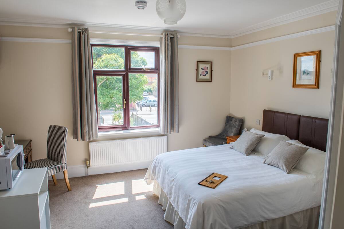 A bedroom with a bed, a chair, a desk, a window with curtains, and a radiator.