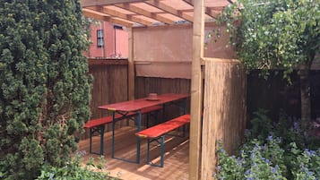A wooden pergola with a table and benches in a garden area.
