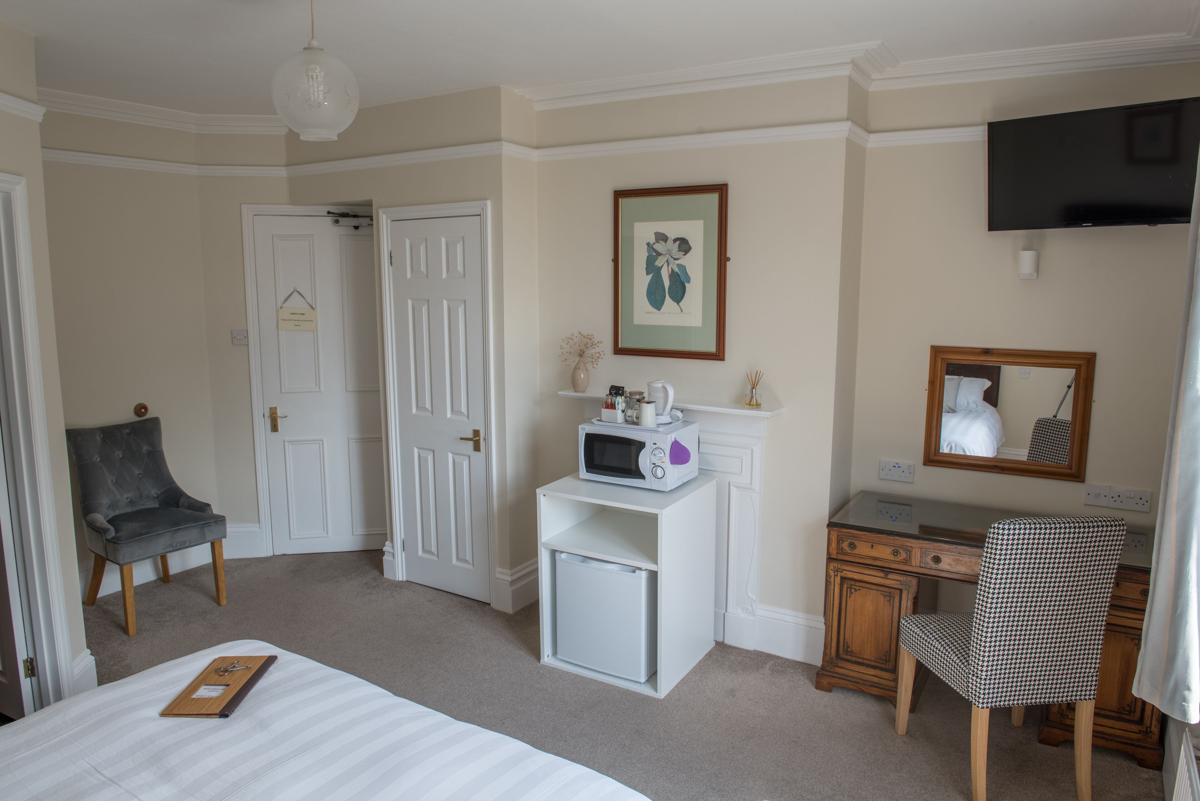 A bedroom with a bed, a desk, a chair, a microwave, a television, and a door.