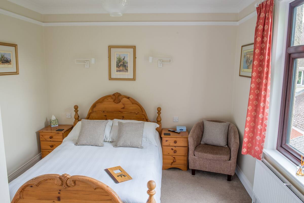 A bedroom with a wooden bed, two nightstands, a chair, and a window with a curtain.