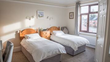 Ein Schlafzimmer mit zwei Einzelbetten, Nachttischen, einem Sessel und einem Fenster mit Blick ins Freie.