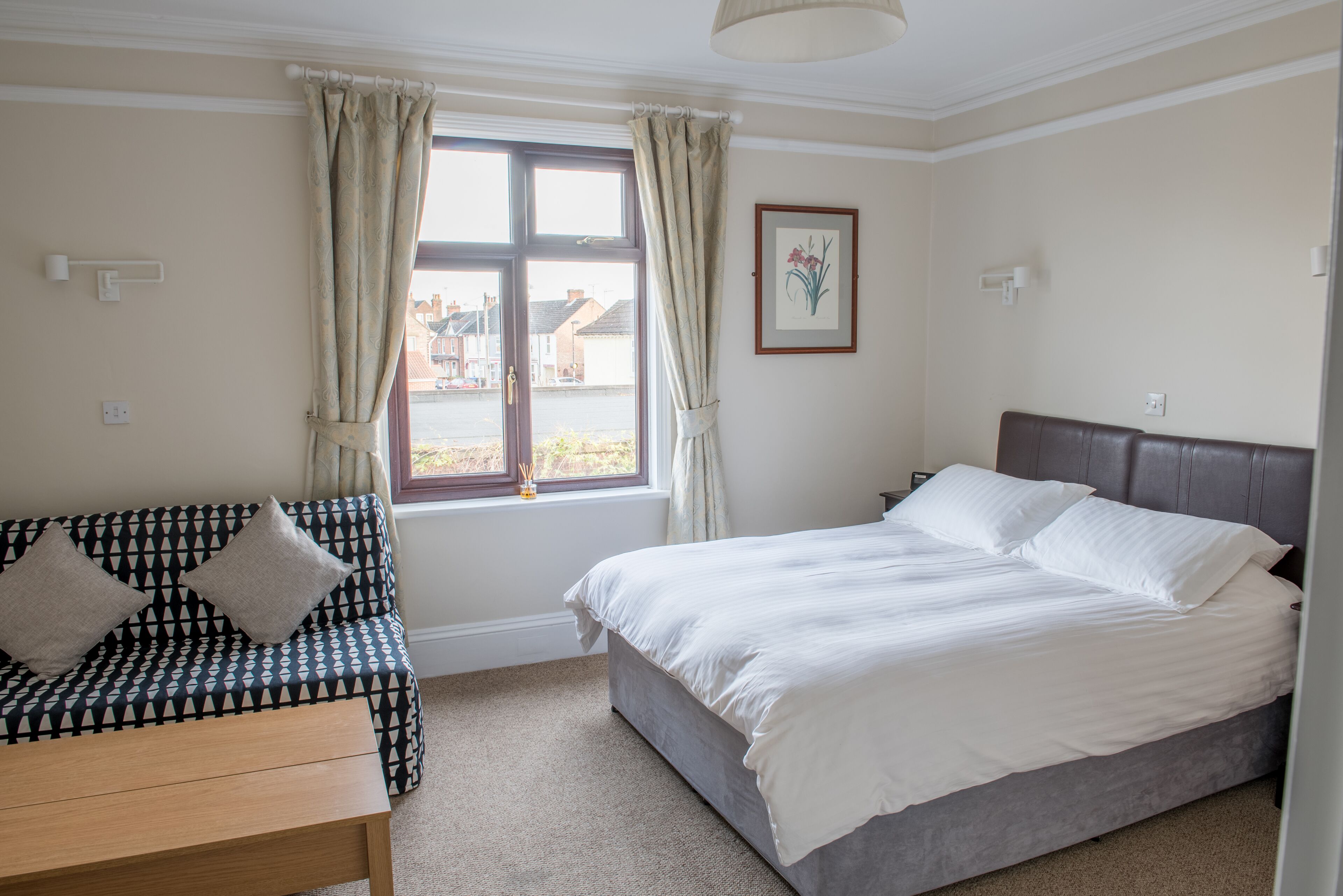 A bedroom with a bed, a sofa, a small table, and a window with curtains.