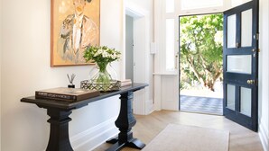 Een hal met een zwarte console tafel, een lijst met een schilderij en een deur die naar buiten leidt.