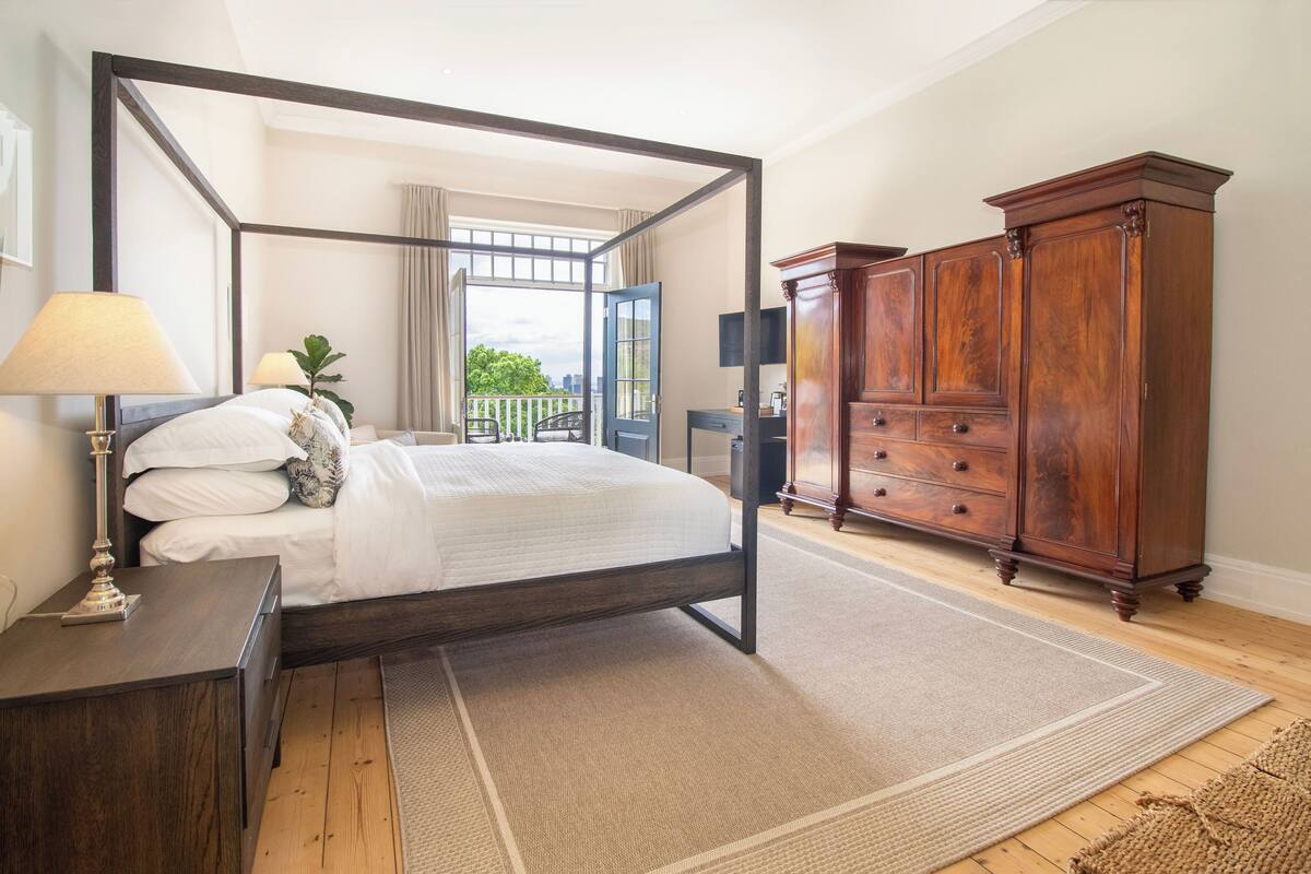 Een hemelbed met uitzicht, een houten garderobe en een klein nachtkastje met een lamp.
